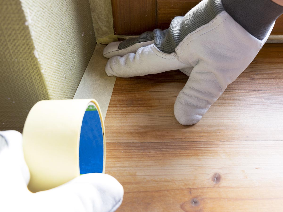 Painter putting tape on hardwood floors around edges of walls